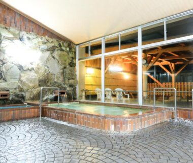 Indoor onsen bath with stone wall, wooden edging and glass doors at Tango Onsen Hashiudosou Kyoto