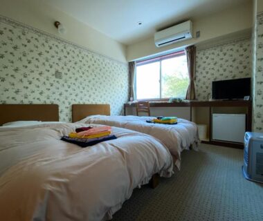 Twin beds with folded robes and TV in room at Tango Onsen Hashiudosou Kyoto