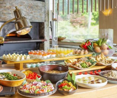 Assorted buffet dishes and desserts on a wooden table inside bright dining room with garden view
