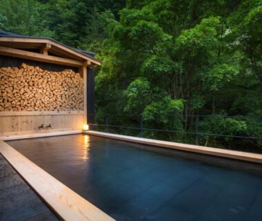 Outdoor wooden onsen bath with stacked firewood beside forest at Tateshina Shinyu Onsen, Nagano