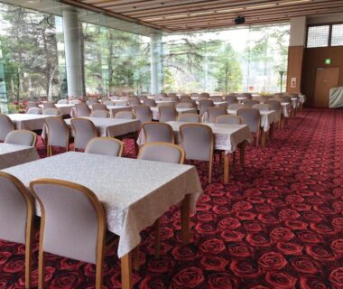 Large dining room with rows of tables and chairs and floor-to-ceiling windows overlooking trees