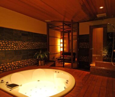 Warm-lit room with sunken round wooden bath and pebble-accent wall at Tatsumikan, Gunma, Japan