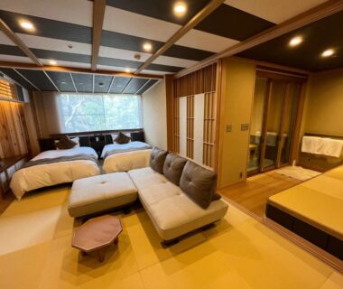 Tatami-floored room with twin beds, low sofa and visible wooden bath area at Tatsumikan, Gunma, Kantō