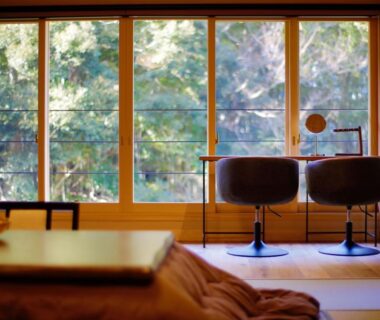Tatami room with futon, low table and chairs facing wooded window at Tatsuta Ryokan, Shizuoka