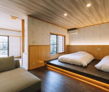 Japanese-style room with futon on raised wooden platform, low sofa and shoji sliding doors to garden