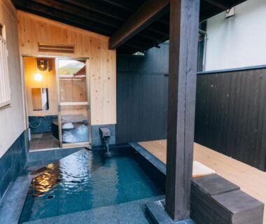 Sheltered stone onsen bath with wooden deck and sliding doorway at Tawarayama Onsen Ryokan Minawa, Kumamoto