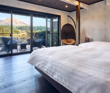 Room with low bed, hanging rattan chair and balcony framing mountain view at Tawarayama Onsen Ryokan Minawa, Kumamoto