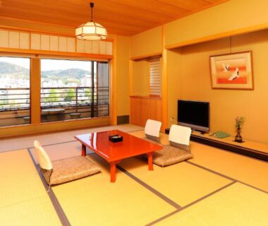Tatami room with low table, floor chairs and balcony overlooking hills at Tazuru ryokan in Kyoto