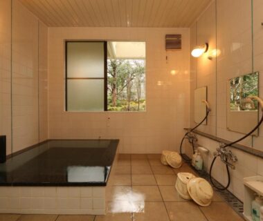 Tiled indoor bath with soaking tub, shower stations, stools and window to greenery at Teiensaryo Yamanakako
