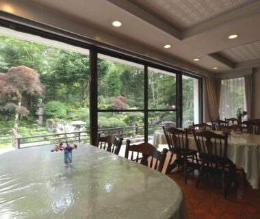 Dining room with set tables and large windows overlooking a green landscaped garden at Teiensaryo Yamanakako Yamanashi