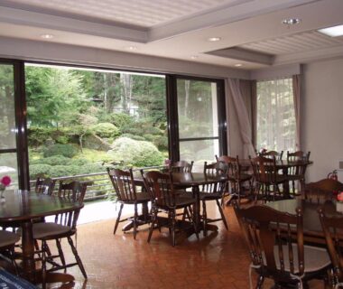 Dining area with wooden tables and chairs overlooking a manicured garden through large windows at Teiensaryo Yamanakako, Yamanashi