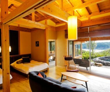 Spacious timber-beamed room with low beds, sofa and large sliding doors opening onto a landscaped garden view in Mie