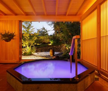 Indoor wooden onsen bath with soft purple light and garden view through shoji screens