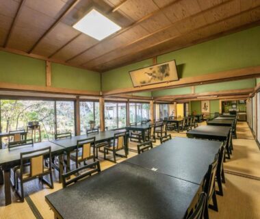 Long tatami dining room with black lacquer tables, chairs, and garden-facing windows at Temple Lodging Shukubo Kakurinbo, Yamanashi