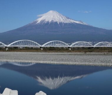 Snow-capped Mount Fuji reflected in calm river with arched bridge near Temple Lodging Shukubo Kakurinbo, Yamanashi