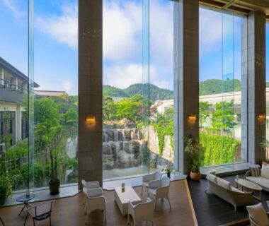 Lounge with floor-to-ceiling windows overlooking courtyard waterfall and green hills at Tendo Hotel, Yamagata