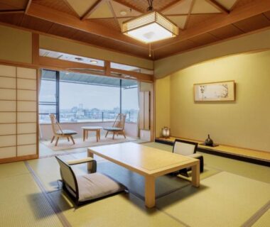 Tatami room with low table, shoji screens, balcony chairs and water view at Tendo Onsen TAKINOYU Yamagata