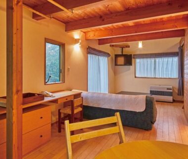 Wooden room with bed, desk and dining table at Tengu Onsen Asama Sanso in Nagano