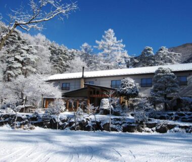Snow-covered ryokan exterior at Tengu Onsen Asama Sanso with frosted trees and blue sky in Nagano