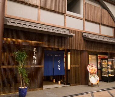 Traditional wooden ryokan entrance with blue noren, potted plant and display case at Tenpyo Ryokan in Nara