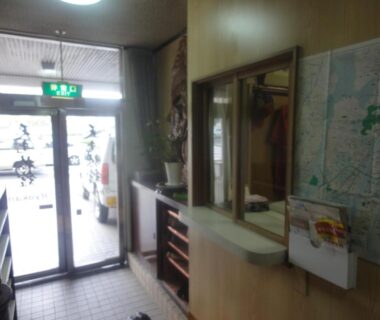 Small ryokan entrance with glass door, shoe racks, reception window and wall map at Tenryu Ryokan, Hiroshima