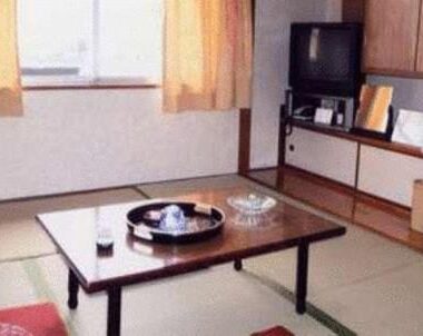 Traditional tatami room with low wooden table, cushions, TV and cabinet at Tenryu Ryokan in Hiroshima