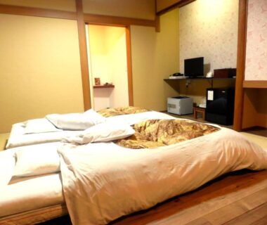 Futon bedding on wooden floor with low TV and shelving at Tenryuso in Chiba, Kantō