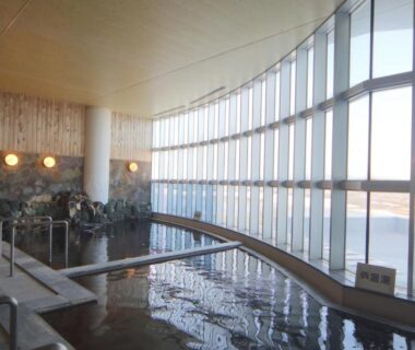 Curved indoor onsen bath with floor-to-ceiling windows and rock feature at Teshio Onsen Yubae Hokkaidō