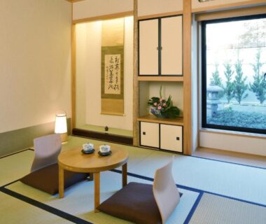Traditional tatami room with low round table, floor cushions, tokonoma alcove and garden view through sliding window