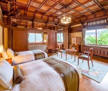 Spacious twin bedroom with ornate wood ceiling, low table and large windows overlooking greenery at The Fujiya Hotel, Kanagawa