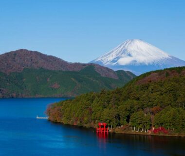 Snow-capped Mount Fuji above a blue lake with shoreline torii and forested hills near The Fujiya Hotel, Kanagawa