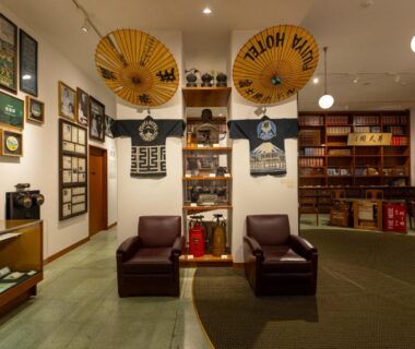 Ryokan lobby with two leather chairs, wagasa umbrellas, framed art and book-lined shelves at The Fujiya Hotel, Kanagawa
