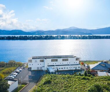 White waterside ryokan building by Amanohashidate sandbar and bay in Kyoto with parking and distant mountains