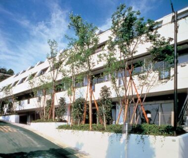 Multi-story ryokan facade with balconies and staked young trees along street in Atami, Shizuoka