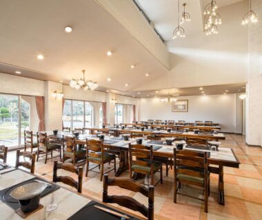 Spacious ryokan dining room with wooden tables, chairs, chandeliers and large windows overlooking garden at The Gran Resort Kinosaki Hyōgo