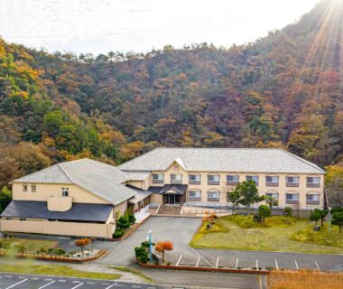 Ryokan building framed by forested hillside with parking area and sunlit slopes in Hyōgo, Kansai