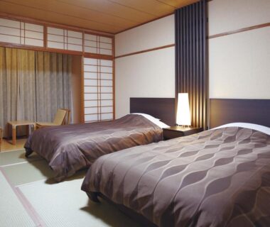 Tatami room with twin beds, shoji screens and bedside lamp at The Gran Resort Kinosaki in Hyōgo, Kansai