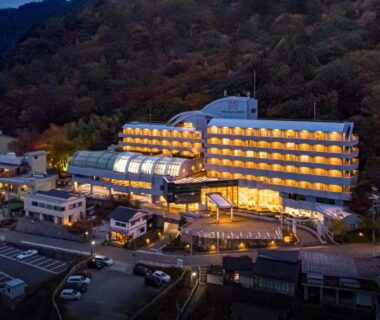 Illuminated multi-story ryokan on hillside at dusk with parking and surrounding buildings in Hyōgo, Kansai