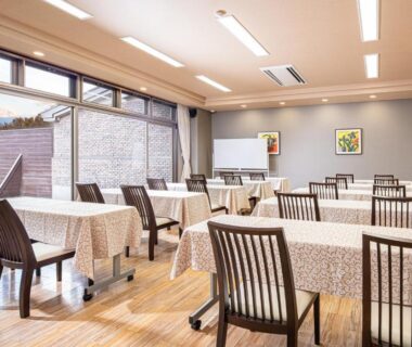 Bright dining room with tablecloth-covered tables, wooden chairs and floor, large windows with mountain views