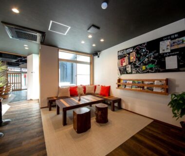 Ryokan lounge with low table, red cushions, wooden stools and large windows at The RYOKAN O, Gifu