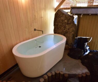 White freestanding soaking tub beside wood-paneled wall and stone floor at おこもりの宿 夢流し, Gifu Chūbu