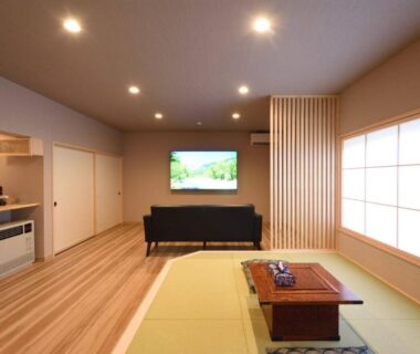 Spacious tatami area with low table, sofa, shoji screen and wall-mounted television in Gifu ryokan room
