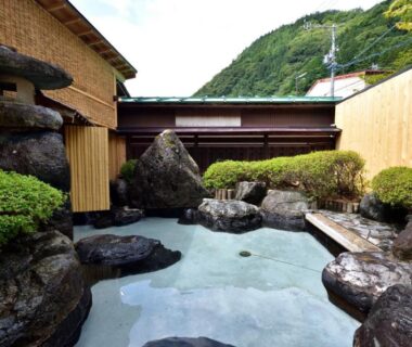 Rock-lined outdoor onsen with bamboo fencing and mountain backdrop at おこもりの宿 夢流し in Gifu