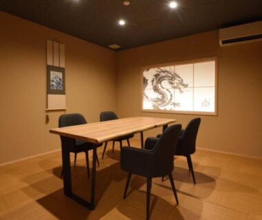 Tatami floored room with wooden table, four chairs, shoji panel with dragon artwork and alcove with hanging scroll