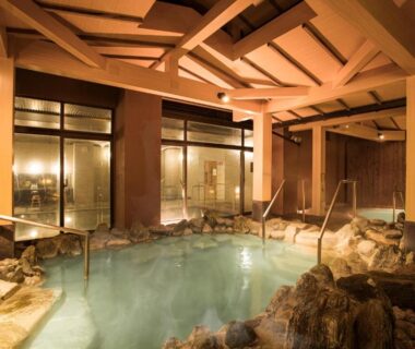 Indoor onsen with wooden beams and stone edging at Toba International Hotel Shiojitei in Mie