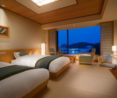 Tatami-floored twin room with low wooden furniture and large window showing evening landscape