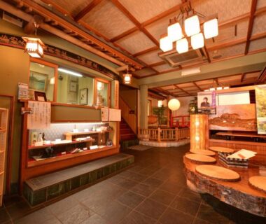 Warm ryokan lobby with wooden beams, display shelves, seating and traditional lighting at Togakubo Kanagawa Kantō