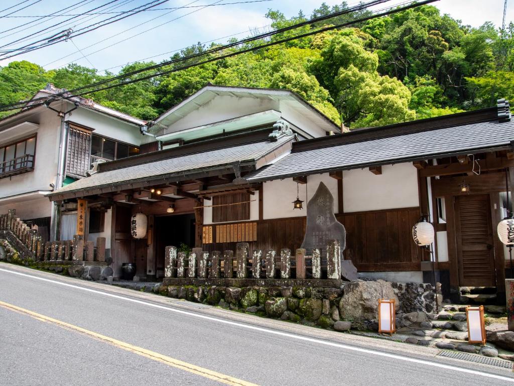 Street front ryokan entrance Togakubo Kanagawa Traditional wooden ryokan exterior with lanterns and stone markers beside roadside and green hillside in Kanagawa