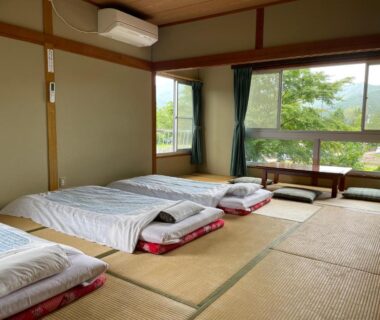 Traditional tatami room with futons and low seating, window overlooking tree-lined hills in Yamanashi