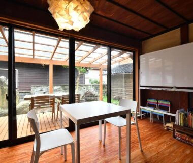 Wood-floored lounge with table and chairs, sliding glass doors opening to a small courtyard garden at Togiso in Ishikawa